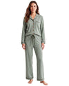 A woman modeling a two-piece pajama set in sage green. The set includes a long-sleeve button-front top with a chest pocket and matching drawstring pants