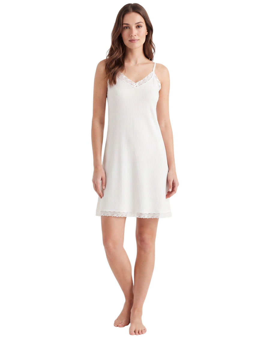 A woman modeling a white ribbed slip nightdress with delicate lace trim at the neckline and hem