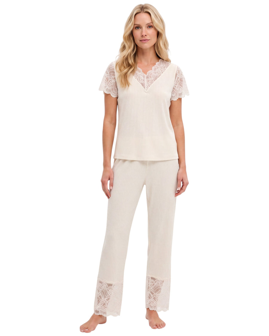 A woman modeling a two-piece cream ribbed pajama set with short lace sleeves and matching lace-trimmed pants