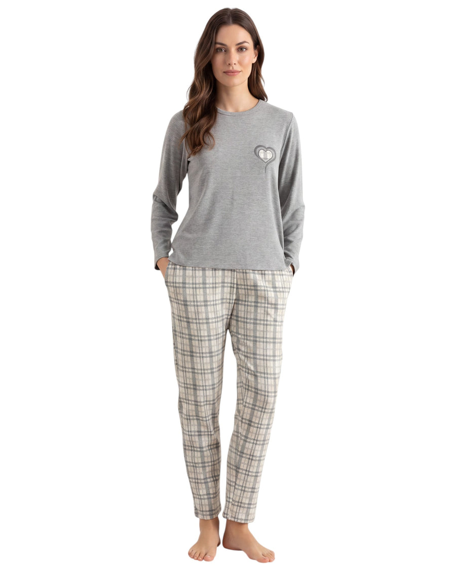 A woman modeling a two-piece pajama set consisting of a heather gray long-sleeve top with a small heart graphic on the chest and beige plaid pants