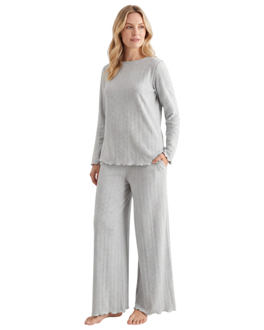 A woman modeling a light gray ribbed two-piece loungewear set consisting of a long-sleeve top with a scalloped hem and matching wide-leg pant