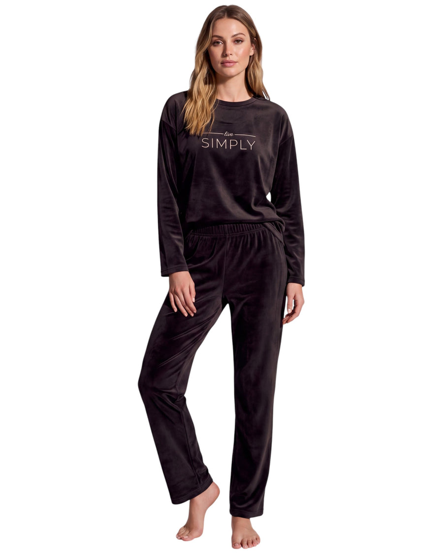 A woman modeling a two-piece black velvet pajama set with a long-sleeve top featuring the word 'SIMPLY' printed in white on the chest, and matching drawstring pants