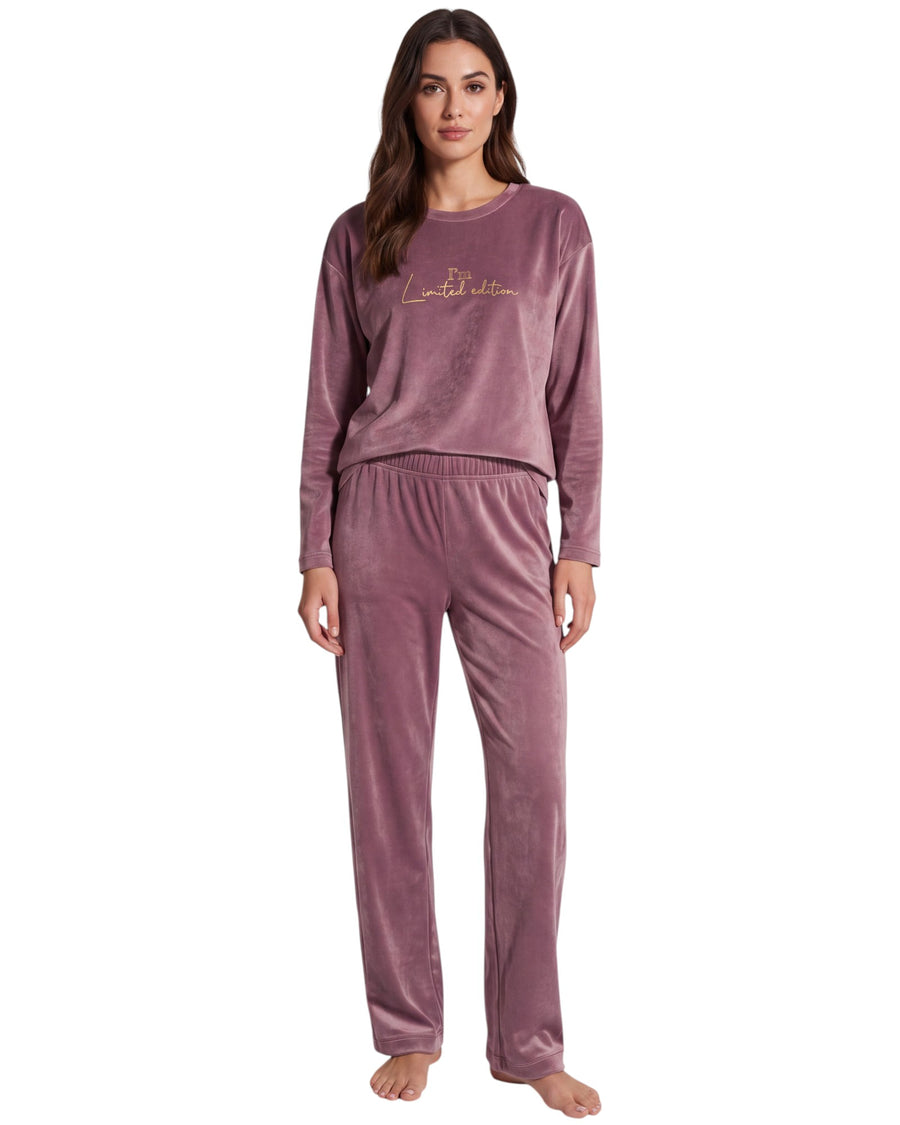 A woman modeling a two-piece velour pajama set in dusty mauve with a small gold embroidered logo on the chest