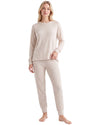 A woman modeling a matching two-piece pajama set in a light beige color, consisting of a long-sleeve crewneck top and matching pants