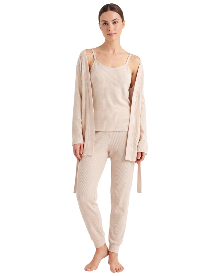 A woman modeling a light beige knit loungewear set consisting of a camisole, matching jogger pants, and a long open-front cardigan