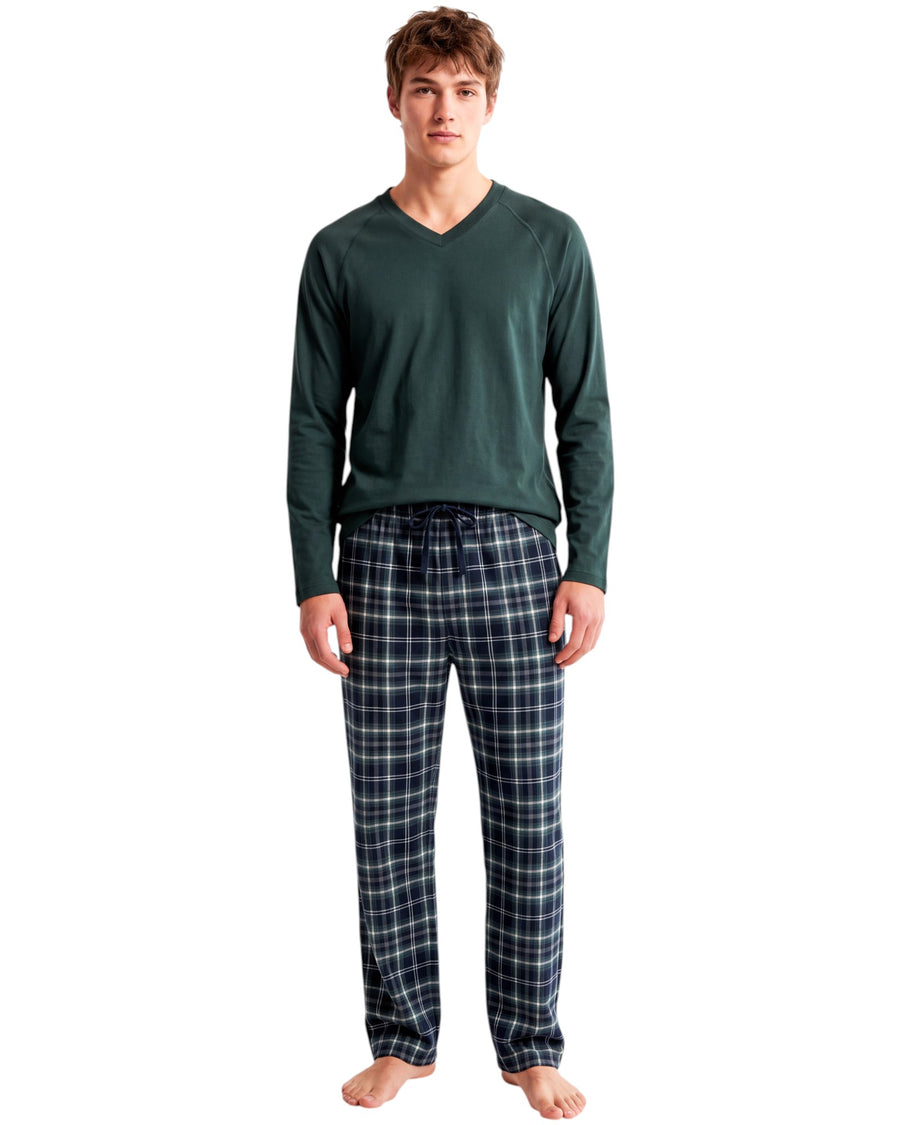A man modeling a two-piece pajama set consisting of a dark green long-sleeve V-neck shirt and navy blue plaid pajama pants