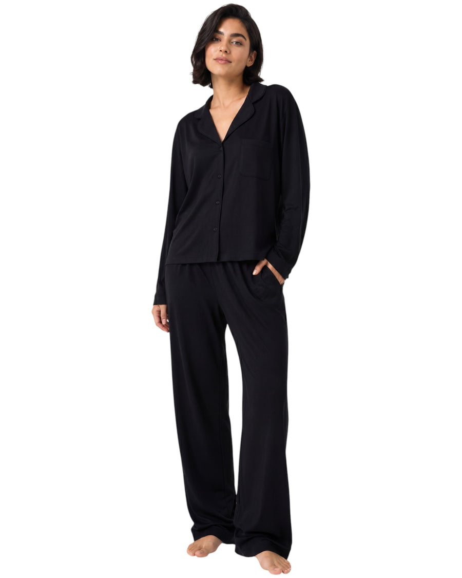 A woman modeling a black two-piece pajama set consisting of a long-sleeve button-front top and matching wide-leg pants