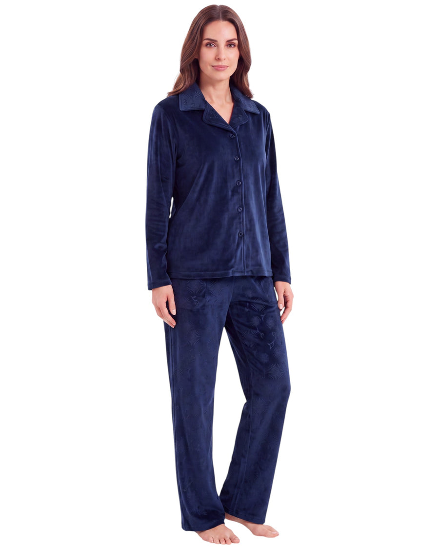 A woman modeling a two-piece navy blue velour pajama set, consisting of a long-sleeve button-up top and matching pants