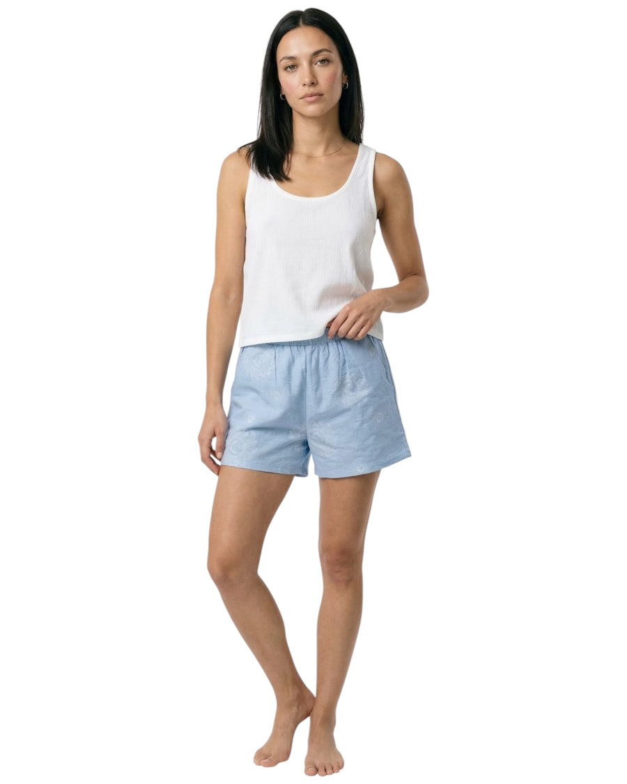 Woman wearing a white tank top and light blue shorts with sun prints