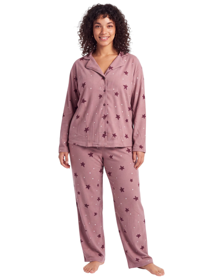 A woman modeling a two-piece pajama set in dusty rose pink with an allover star pattern, featuring a long-sleeve button-front top and matching pants