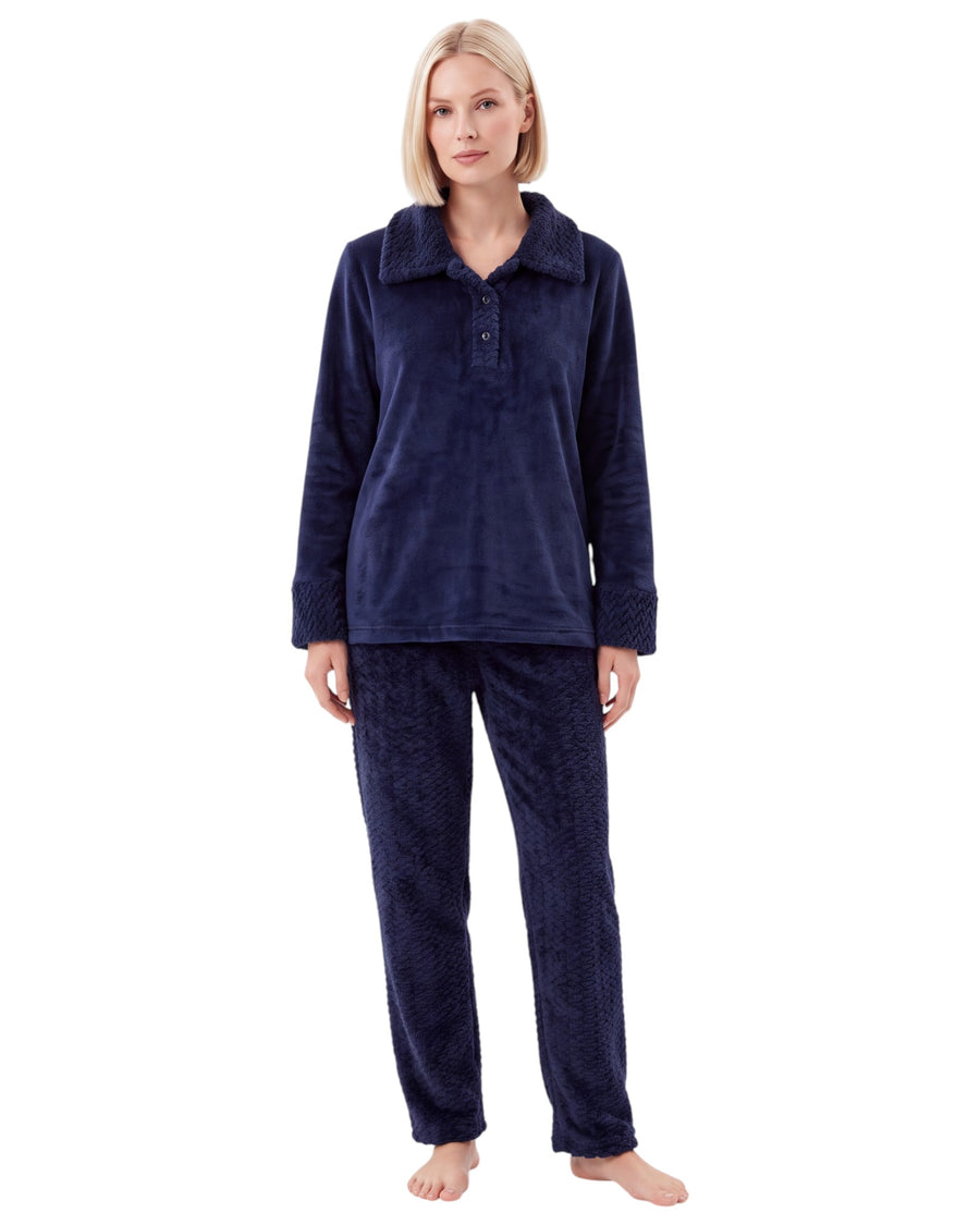 Woman wearing a navy blue plush pajama set featuring a long-sleeve top with a textured collar, buttoned neckline, matching cuffs, and textured long pants.