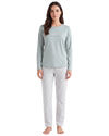 A woman modeling a two-piece pajama set consisting of a light sage green long-sleeve top with a subtle script logo on the chest and white pants with a small gray geometric pattern