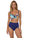 Model wearing a navy high-waist bikini set with abstract multicolor print top, adjustable straps, and supportive structured fit.