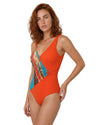 Model wearing a sunset orange one-piece swimsuit with tropical abstract print detail, wrap-style silhouette, and elegant side buckle accent.