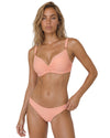Model wearing a peach ruched bikini set with adjustable straps, molded cups, and matching low-rise bikini bottoms.