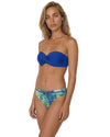Woman wearing a cobalt blue bandeau bikini top with tropical print bikini bottoms in blue and green shades.