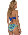 Woman wearing a cobalt blue bandeau bikini top with tropical print bikini bottoms in blue and green shades.