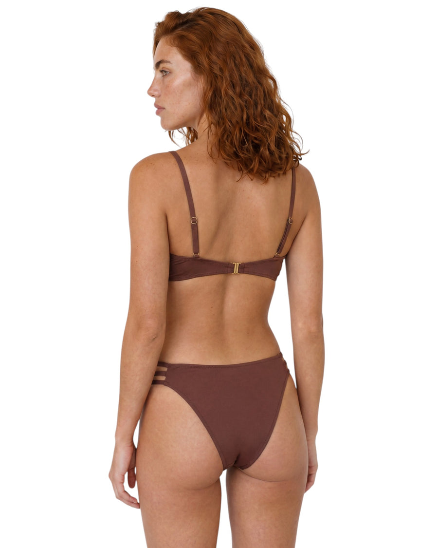 Model wearing a chocolate brown bikini set with gold-tone U-bar detail, adjustable straps, and strappy side bikini bottoms.