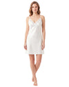 A woman modeling a white slip-style nightgown with thin straps, lace trim at the neckline, and a scalloped hem 