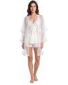 A woman modeling a white lingerie set consisting of a sheer long robe with lace trim, a matching satin slip, and matching lace-trimmed shorts