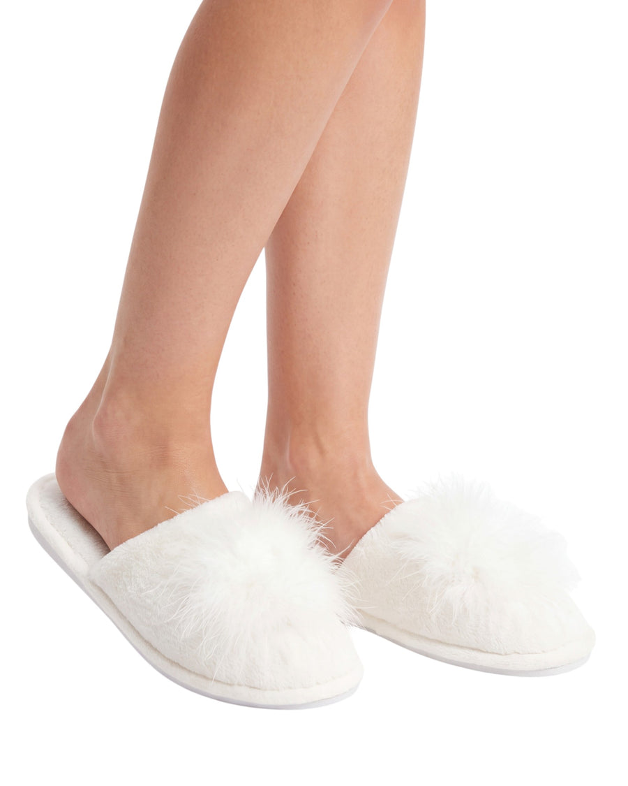 A pair of fluffy white slip-on slippers worn on a person's feet